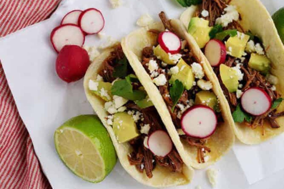 Beef tacos on white parchment with toppings.