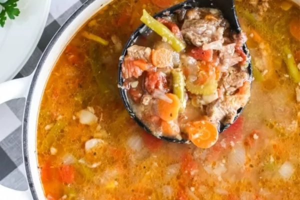 A pot of vegetable beef soup with a ladle.