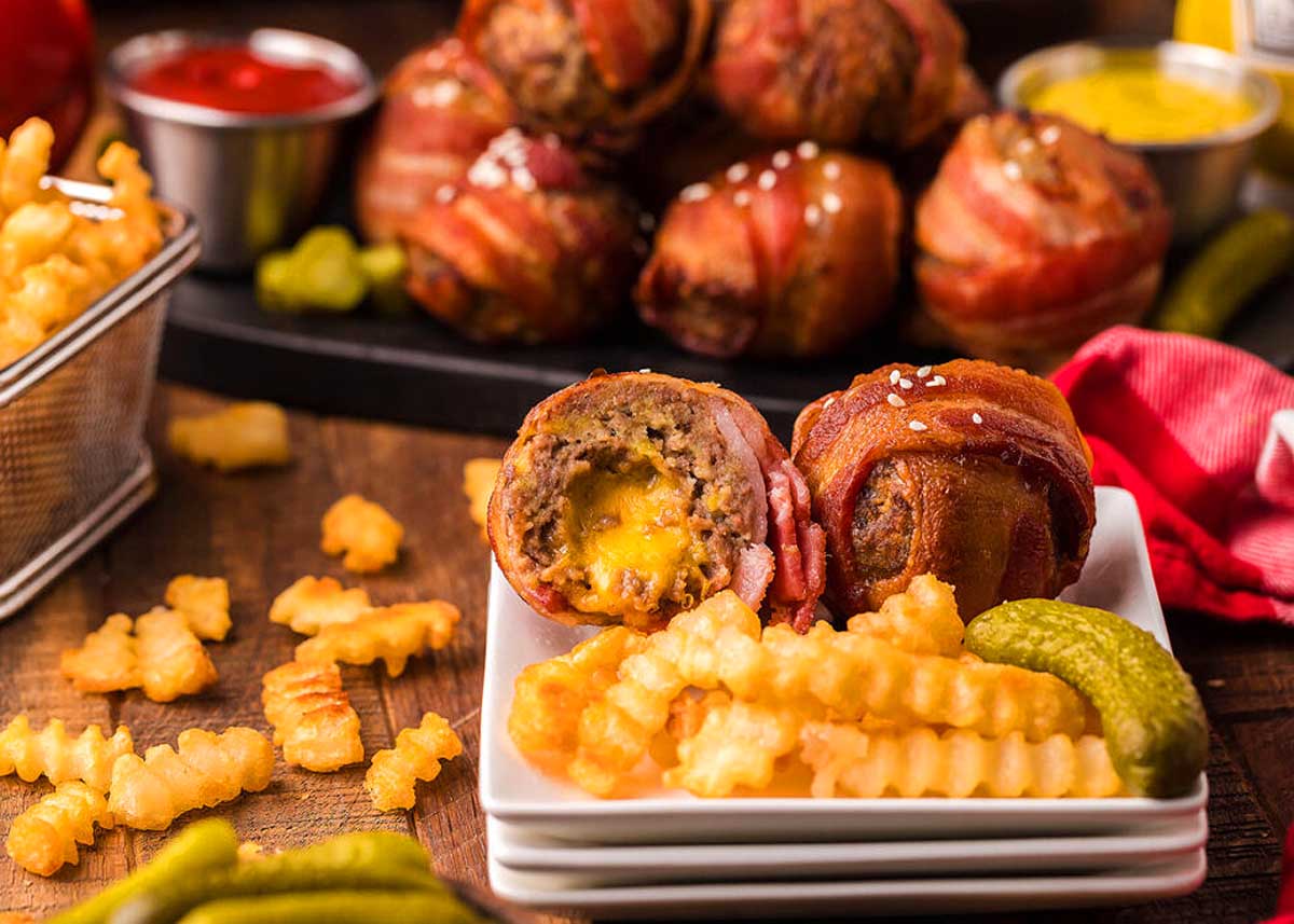 Bacon wrapped cheese burger bits on a plate with fries.