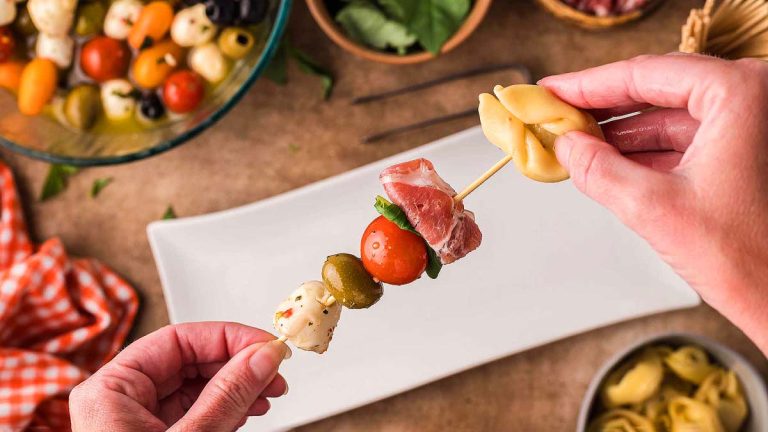 A person is holding an appetizer skewer with meat and vegetables on it.