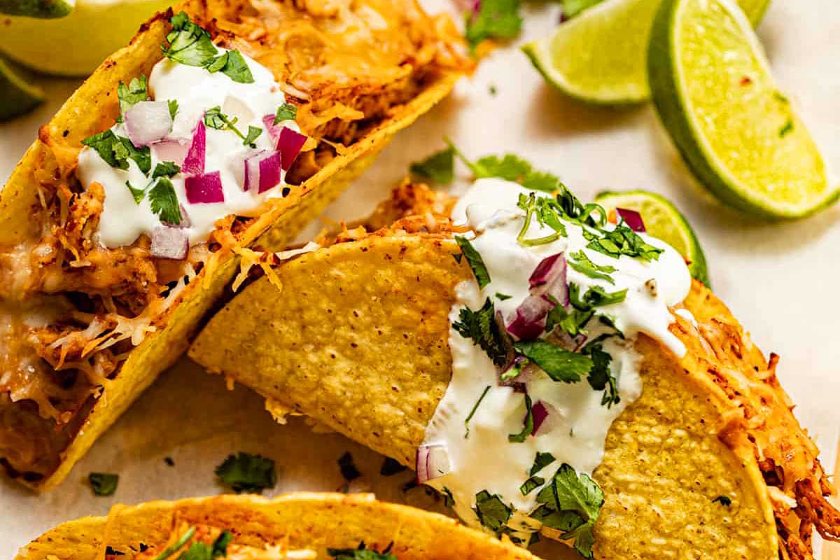 Three chicken tacos with sour cream and lime wedges.