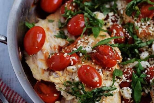 Balsamic chicken in a skillet with tomatoes on top.