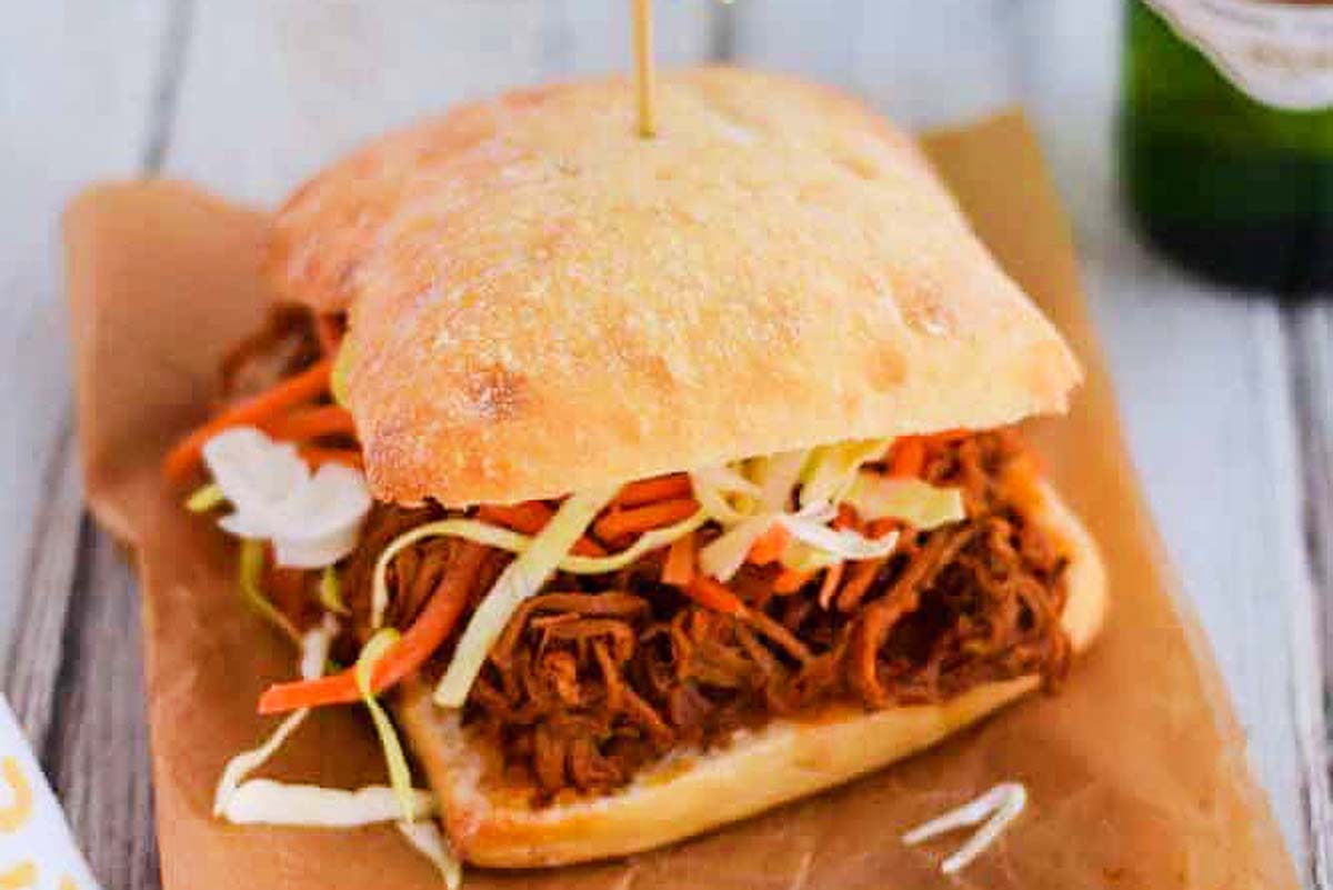 A bun sandwich with bbq pork and shredded vegetabbles.