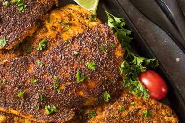 Blackened chicken cutlets on a black plate.