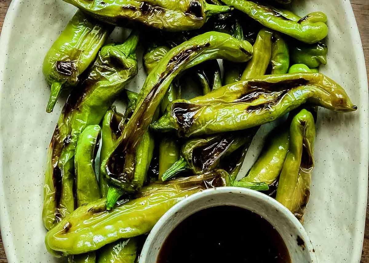 Blistered peppers on a plate with a dipping sauce on the side.