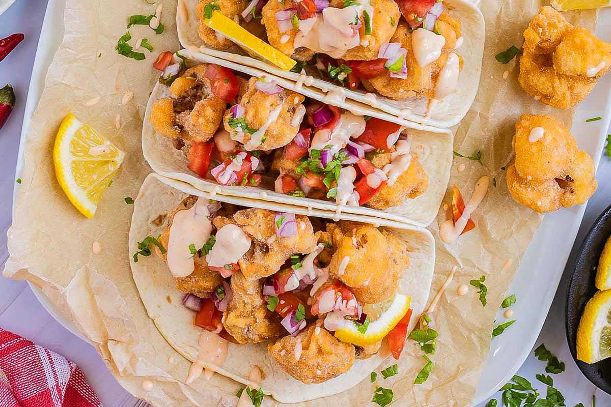 Three fried fish tacos on a white plate.