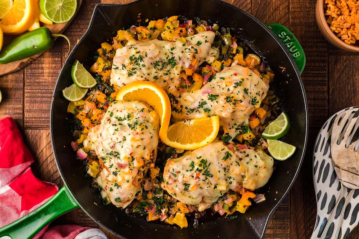 A skillet with chicken breasts on top of them and peppers.