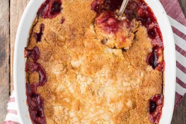 Cherry dump cake in a casserole dish with a spoon.