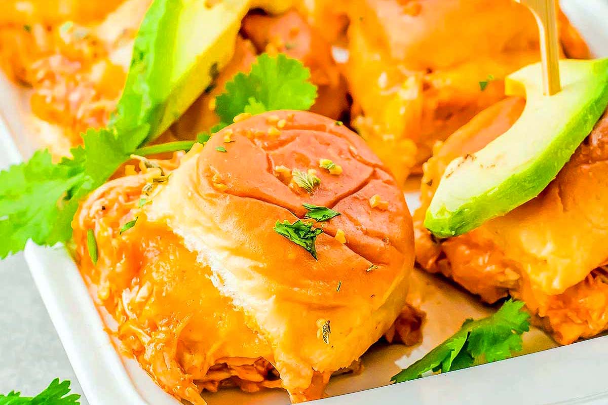 Sliders with an enchilada filling and a slice of avocado on top.