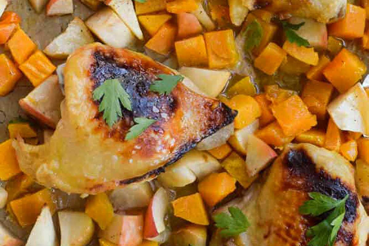 Roasted chicken with apples and carrots on a baking sheet.
