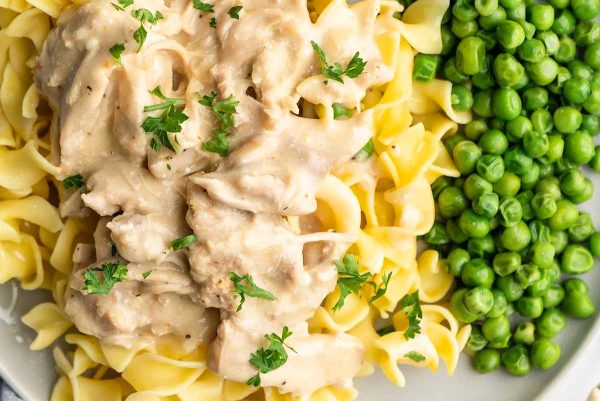 Crockpot chicken with gravy, noodle and peas on a plate.