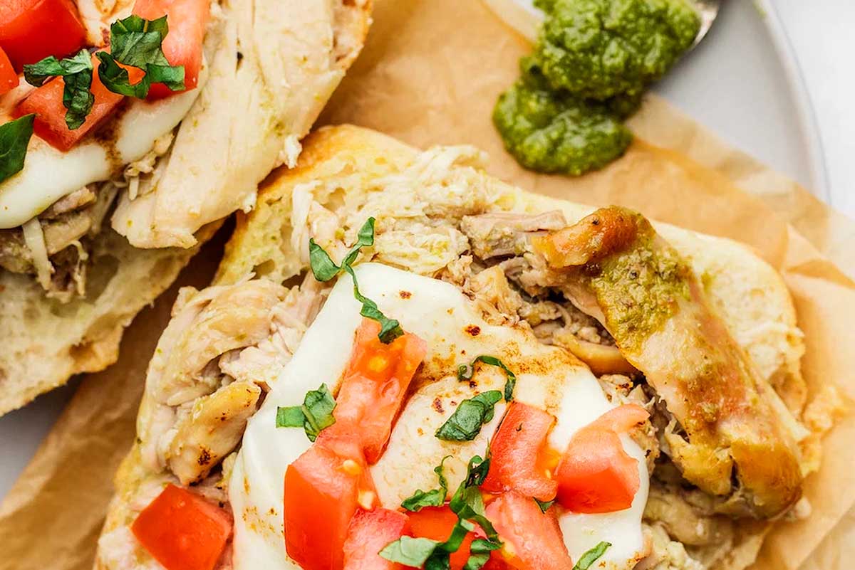 Crockpot pesto chicken on a plate topped with cheese and tomatoes.