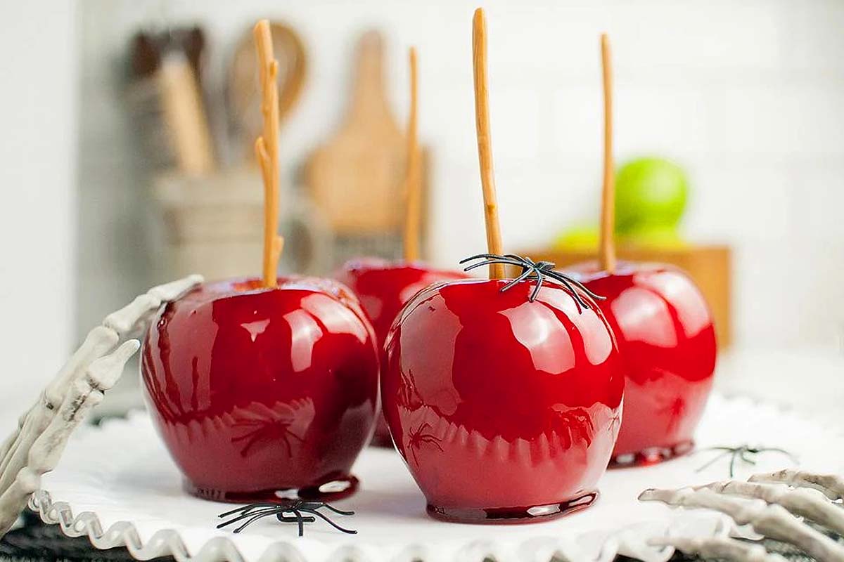 Homemade candy apples on a plate with plastic spiders on them.