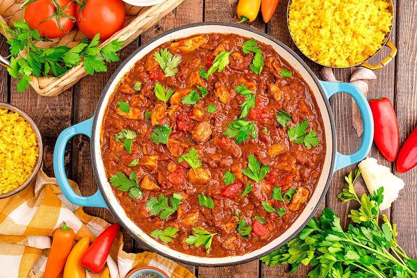 A dutch oven with chicken curry and fresh herbs on top.