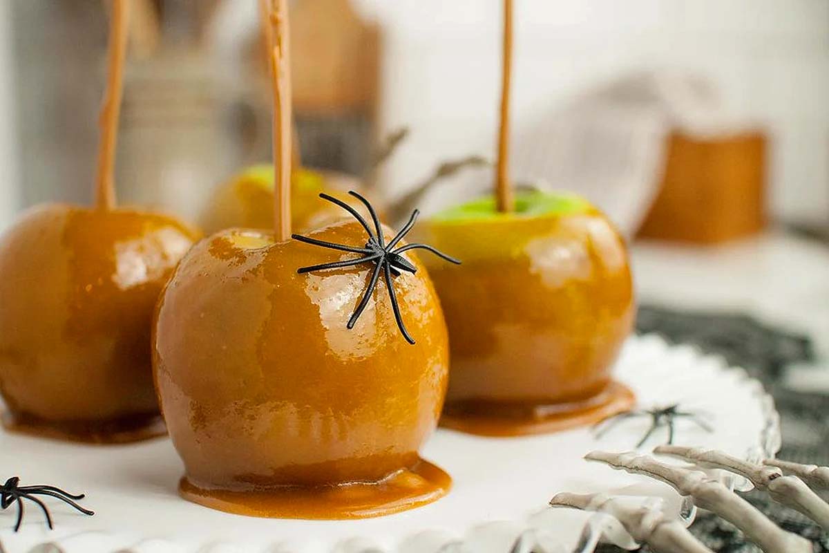 Caramel apples on a tray with plastic spiders on them.