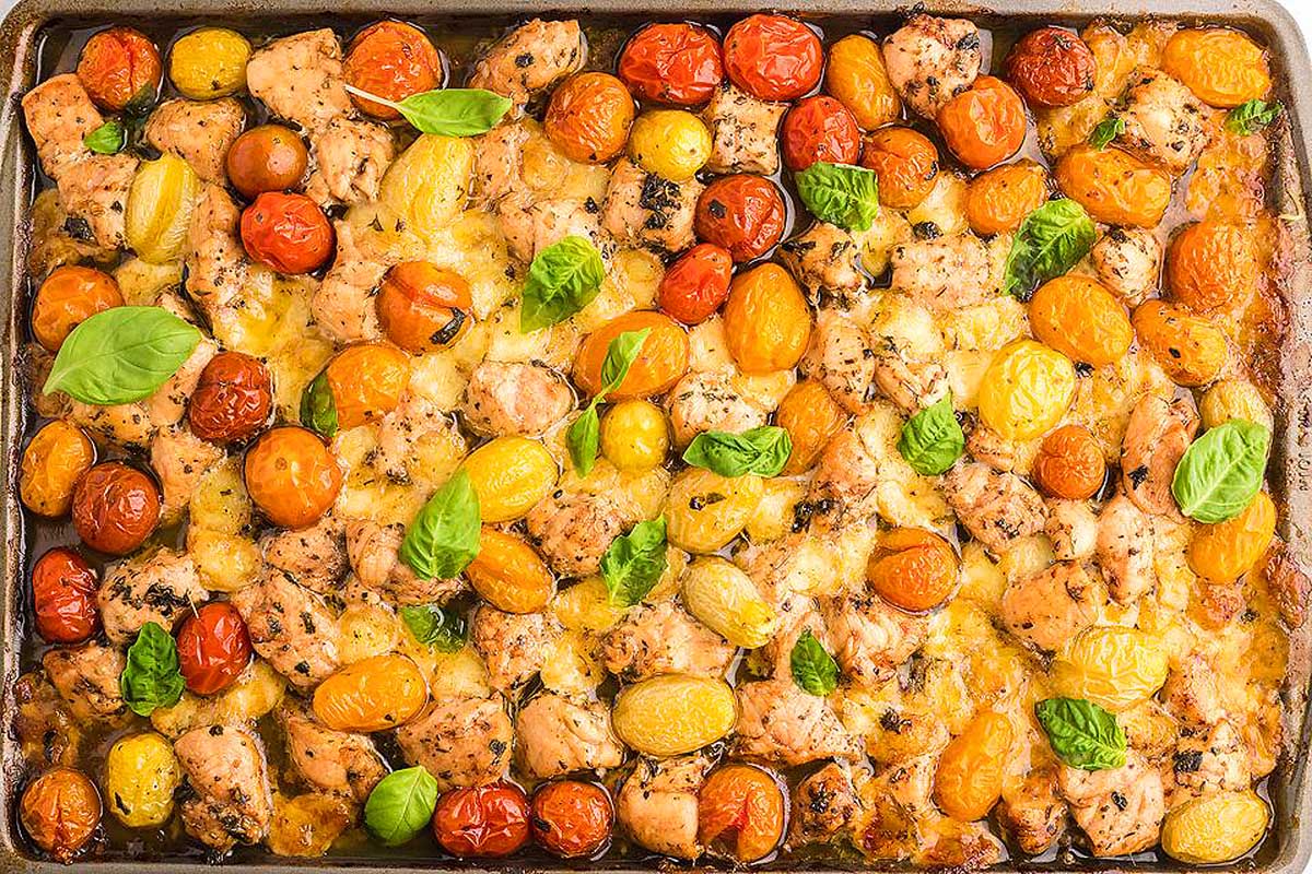 A baking dish with chicken, tomatoes and basil. This is one of the best sheet pan recipes.
