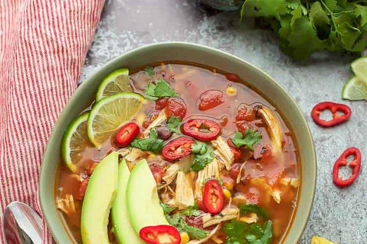A bowl of mexican chicken soup with avocado and lime.
