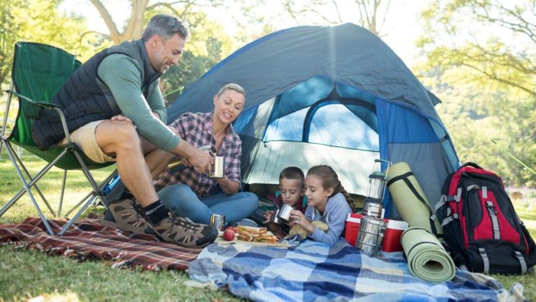Family eating, having snacks and coffee outside the tent at campsite.