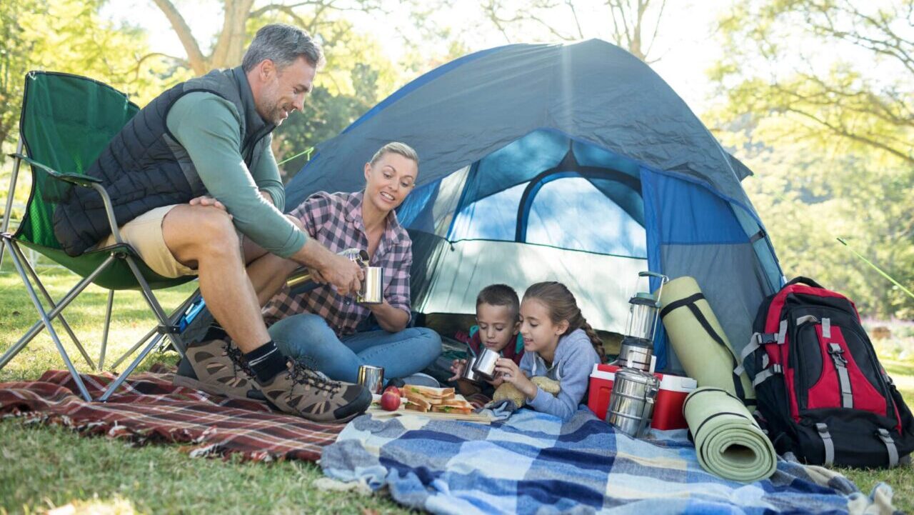 Family eating, having snacks and coffee outside the tent at campsite.