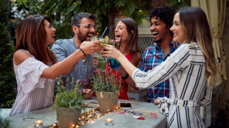 Group of cheerful friends making a toast at cafe's garden with cocktail drinks.