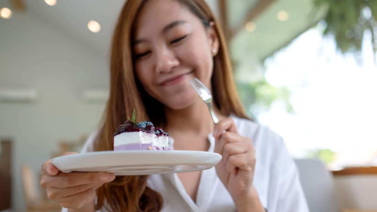 Young woman holding and eating a piece of cheesecake.