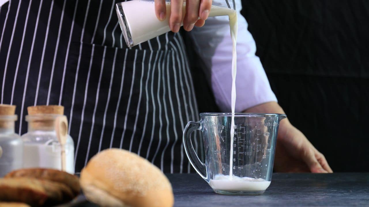 Man pouring milk into a glass measuring cup. 