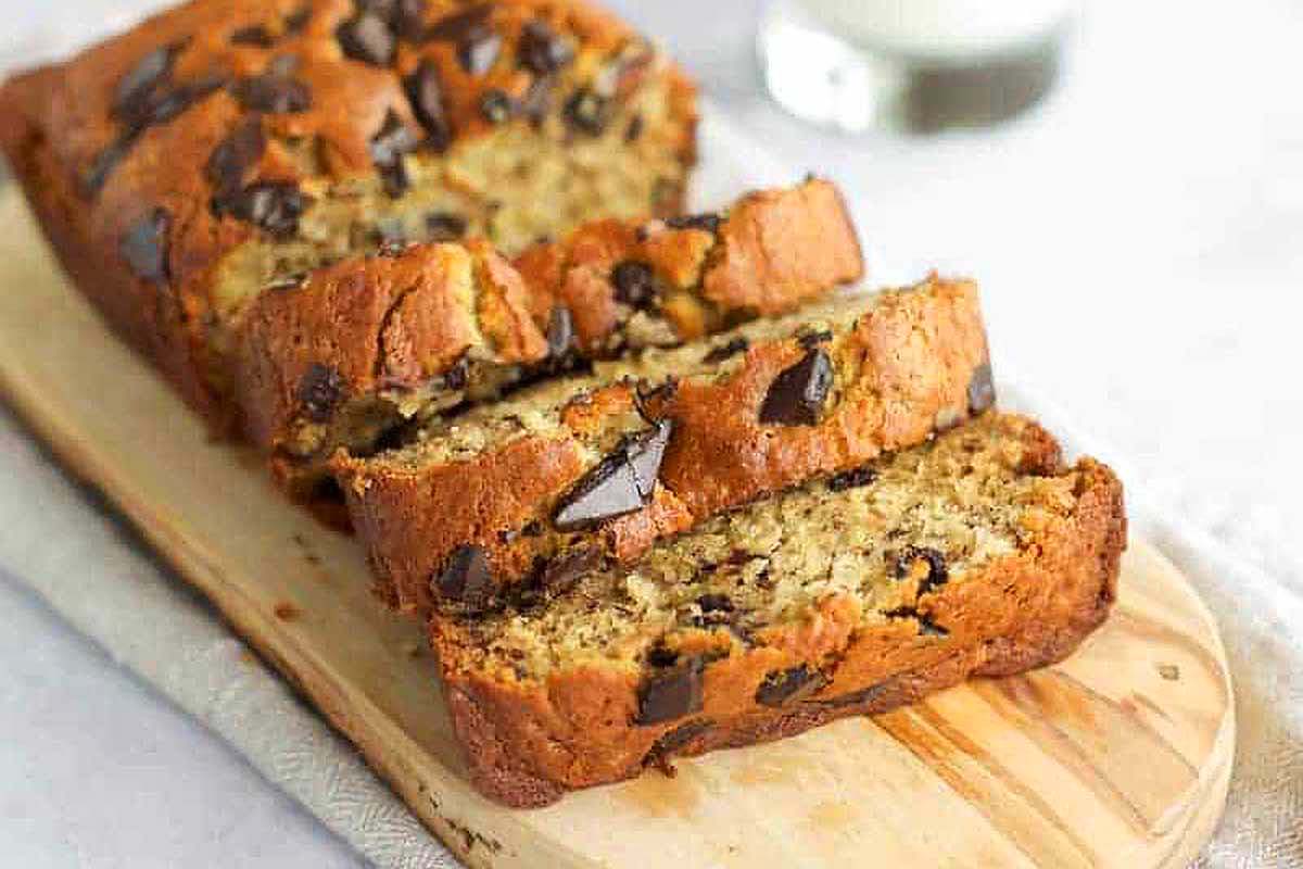 Chocolate chip banana bread on a cutting board with a glass of milk.