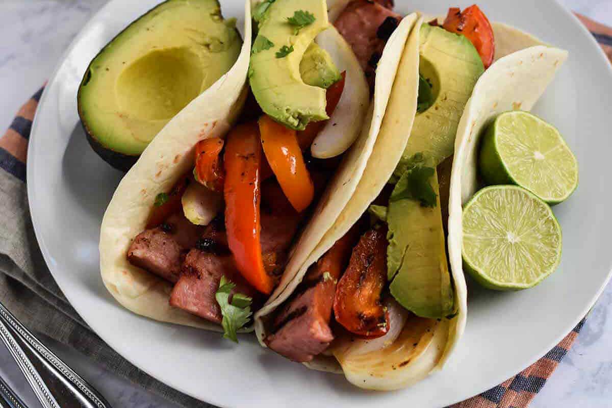 Grilled pork tacos on a white plate.