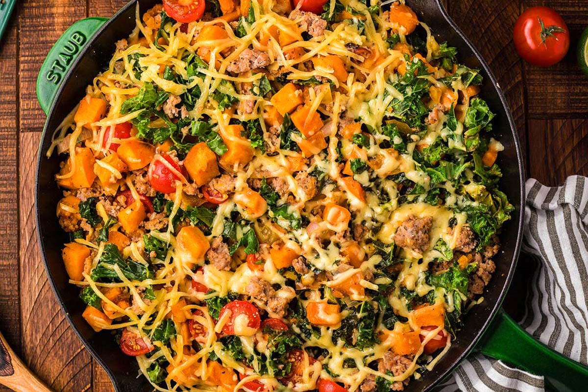 A cast iron skillet with a turkey, kale and sweet potato dish.