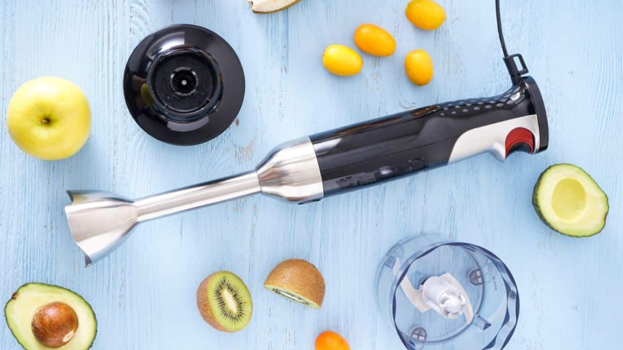 Top view of hand blender and accessories with sliced fruit on a wooden background. 