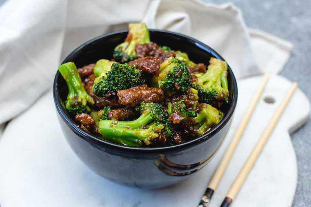 Chinese beef and broccoli in a black bowl with chopsticks.