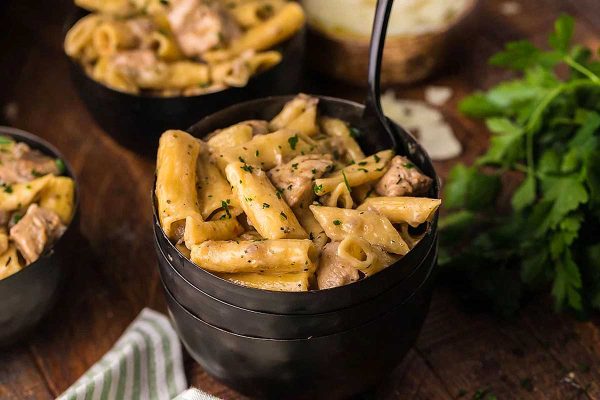 Penne pasta with chicken and parmesan on a wooden table.