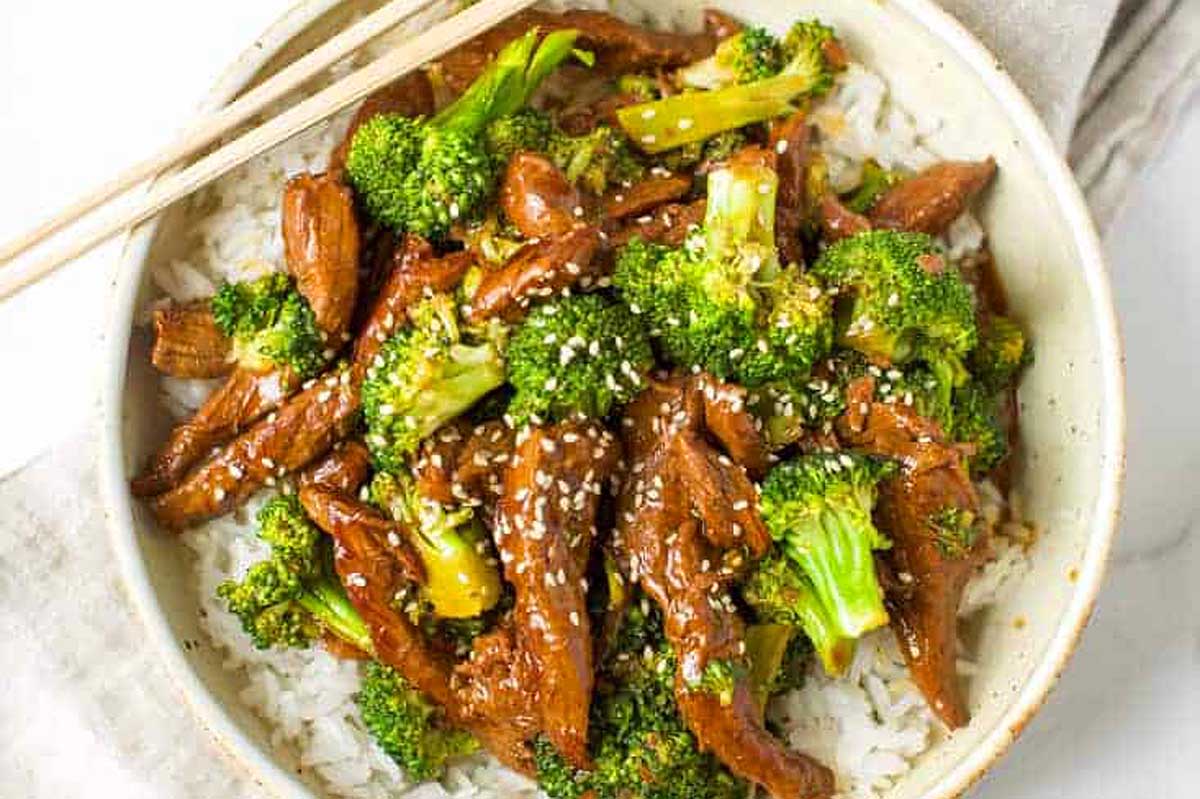 A bowl of beef and broccoli stir fry with chopsticks.