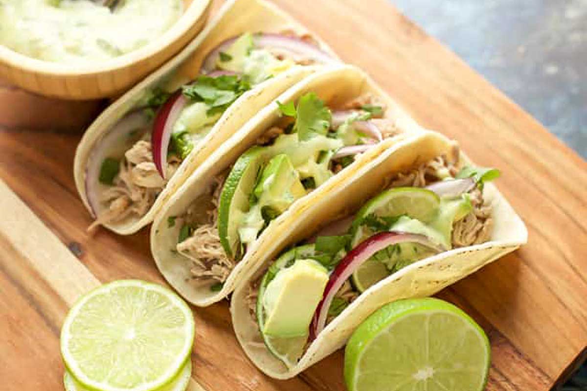 Three tacos on a wooden cutting board.