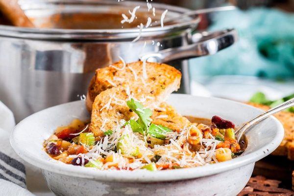 Italian minestrone soup in a while bowl with shredded cheese and toast.