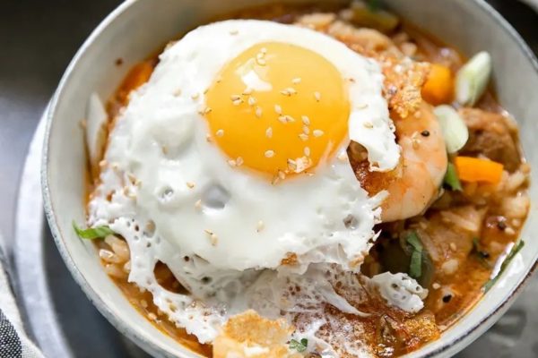 Jambalaya stew in a white bowl with a fried egg on top.