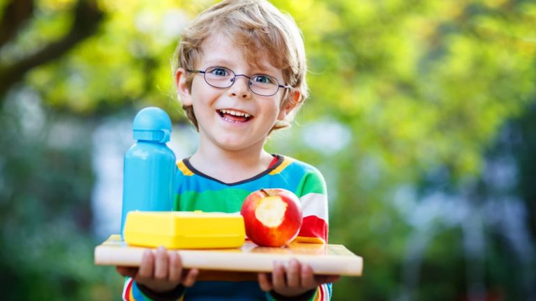 Happy little boy with books, apple and drink bottle on his first day to school.