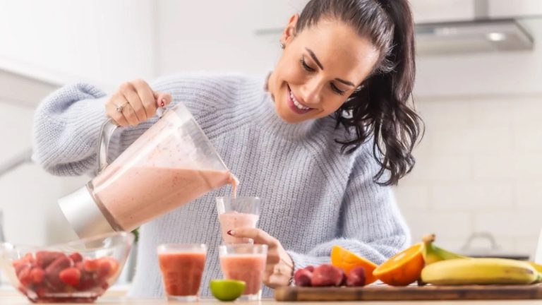 Woman pours fruit smoothie into cups in a kitchen.