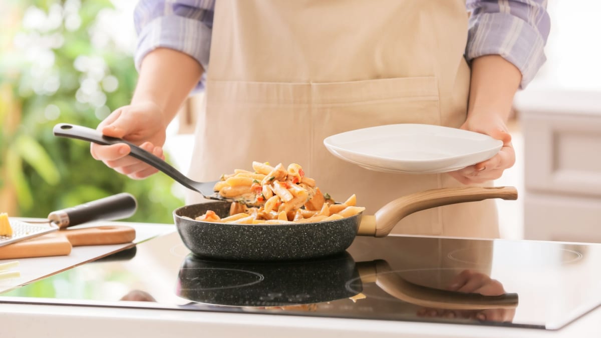Man wearing an apron cooking pasta in a skillet on the stove. 