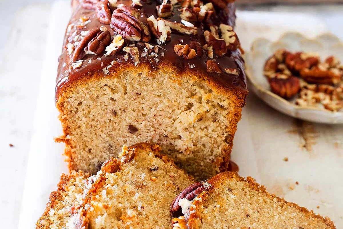 A slice of carrot cake with pecans on a cutting board.