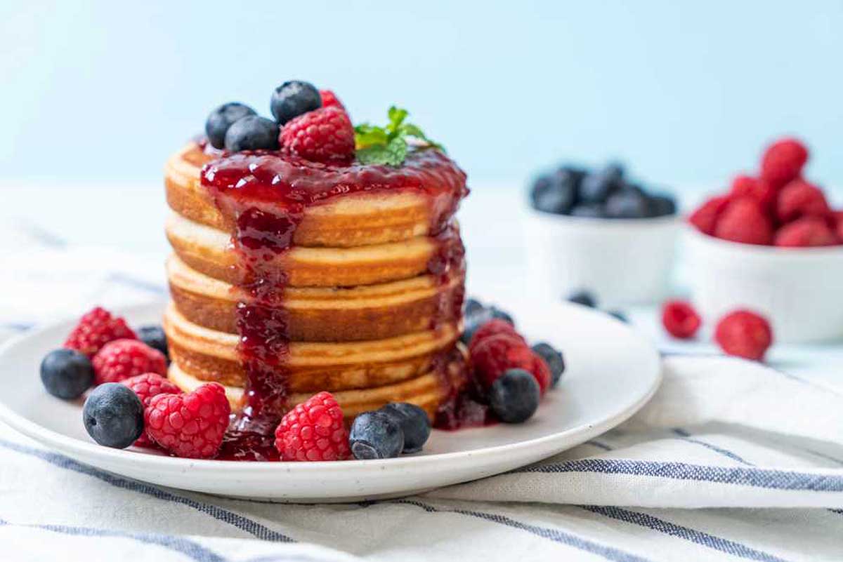 A stack of pancakes topped with berries and syrup.