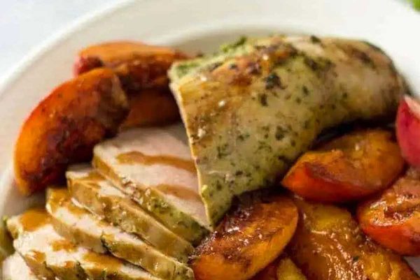 Pork tenderloin on a white plate with gravy and peaches.