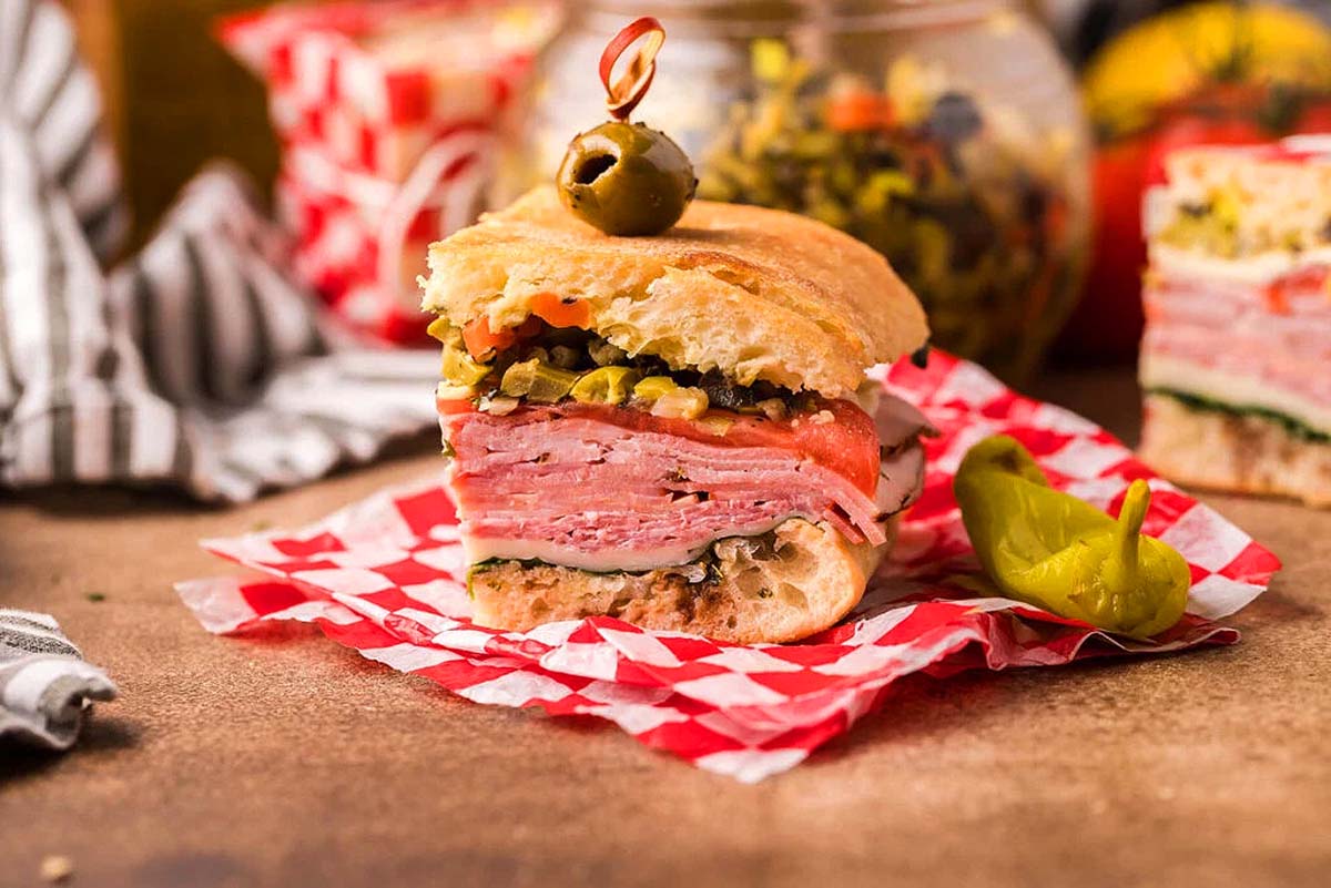 A piece of a pressed Italian sandwich with olive on top.