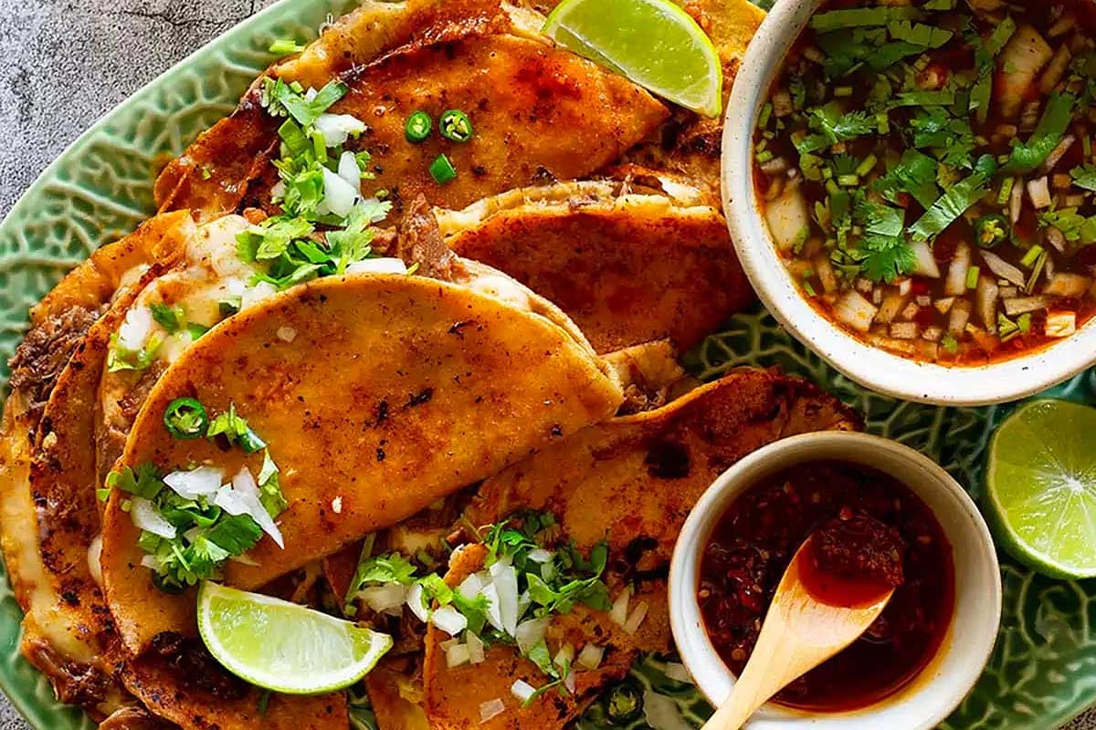 A plate of tacos and a bowl of sauce on a green plate.