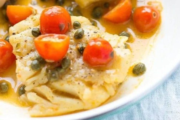 Cod with tomatoes and capers on a white plate.