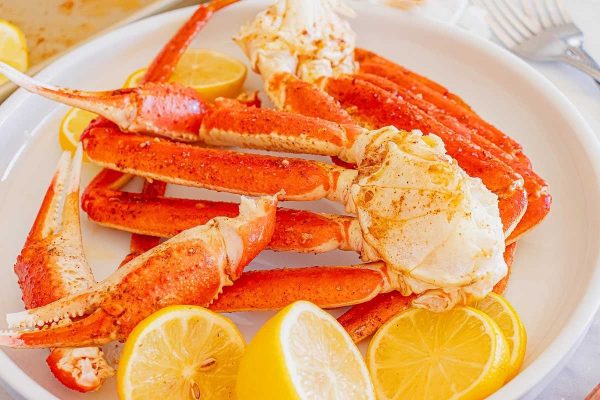 Sheet pan crab legs with lemon on a white plate.
