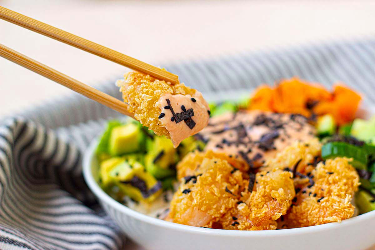 A sushi bowl with crispy shrimp and veggies with rice.