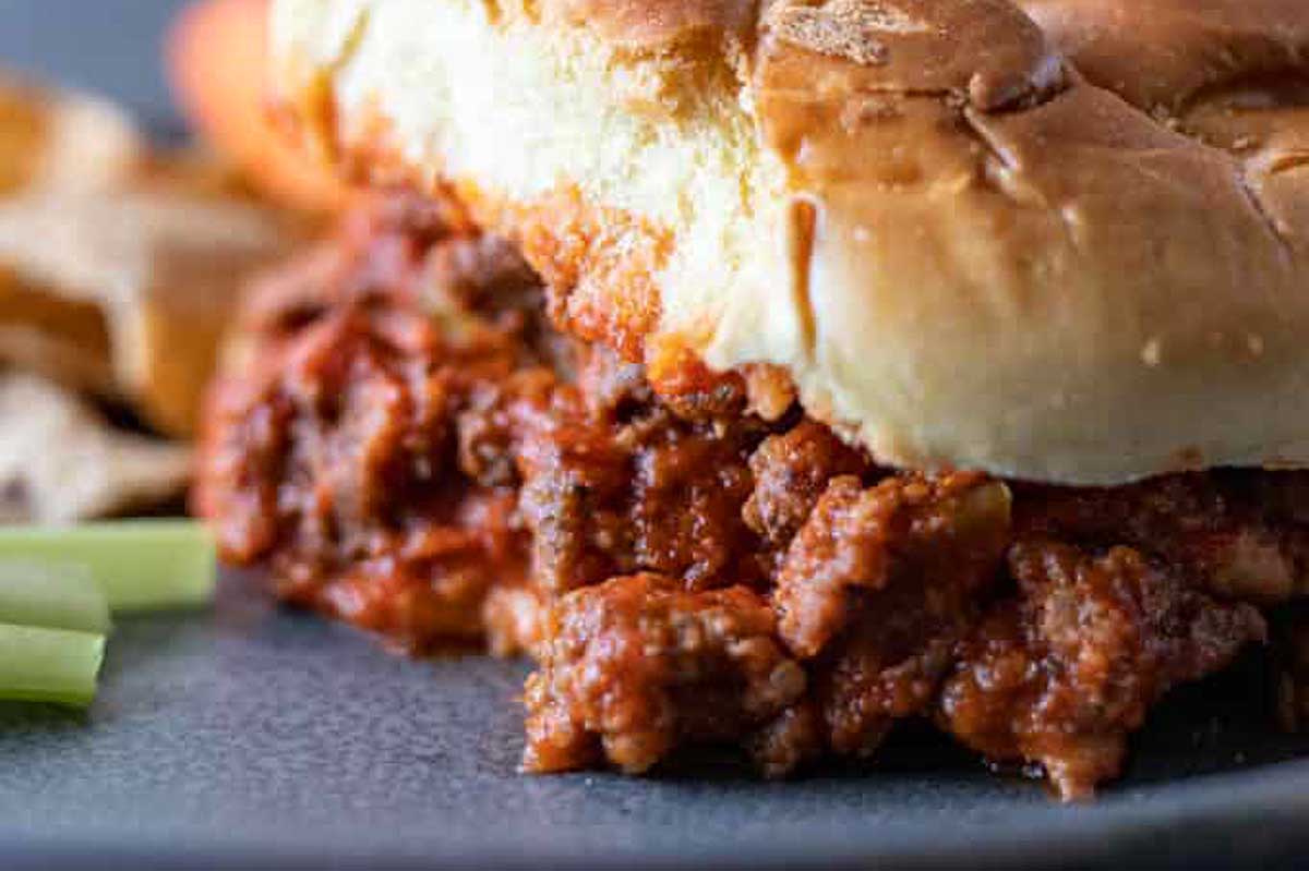 A sloppy joe sandwich on a plate with celery and chips.