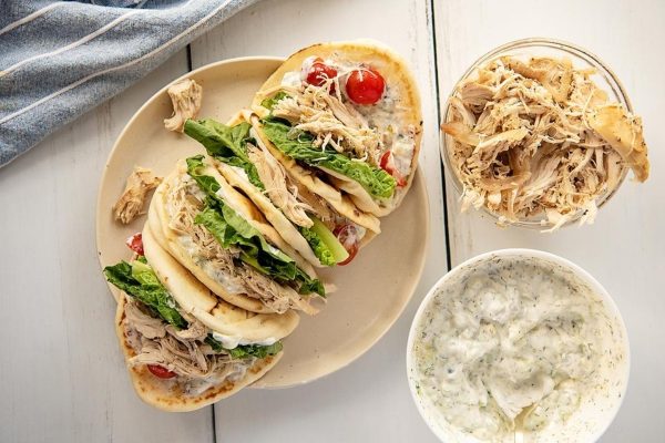 White plate of slow cooker green shredded chicken gyros with tzatziki sauce.