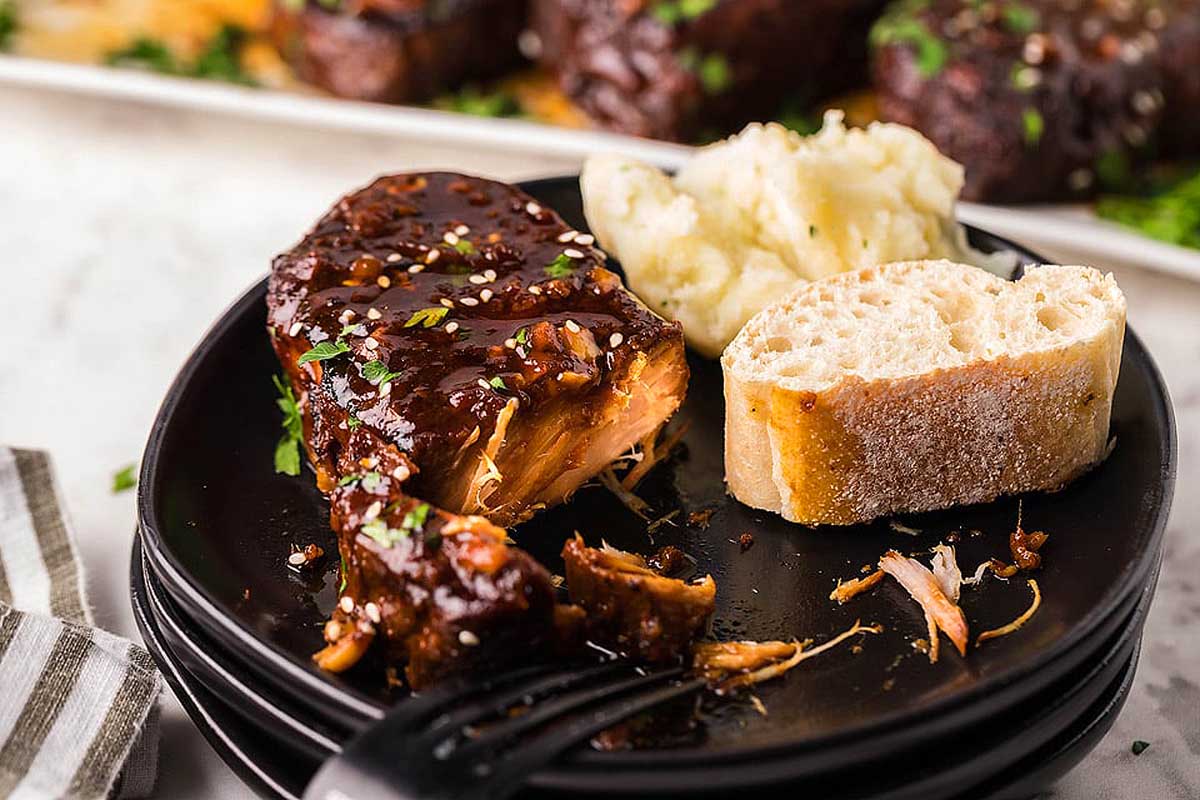 Pork chops on stacked black plates with bread.